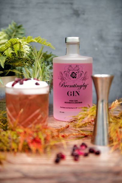 a bottle of pink gin with a pink cocktail on a wooden table