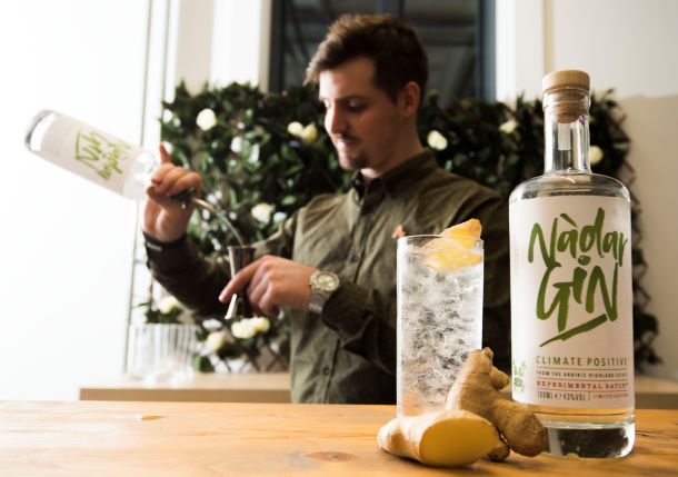 A BOTTLE OF GIN WITH A GIN AND TONIC ON A BAR WITH A BARTENDER MAKING A DRINK IN THE BACKGROUND