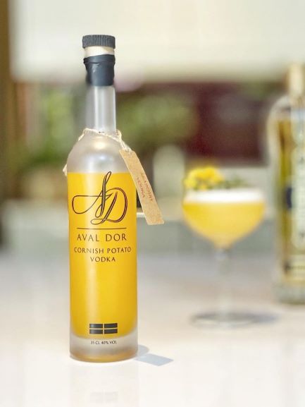 a bottle of colwith farm aval dor seaberry vodka on a white bar with a cocktail in the background