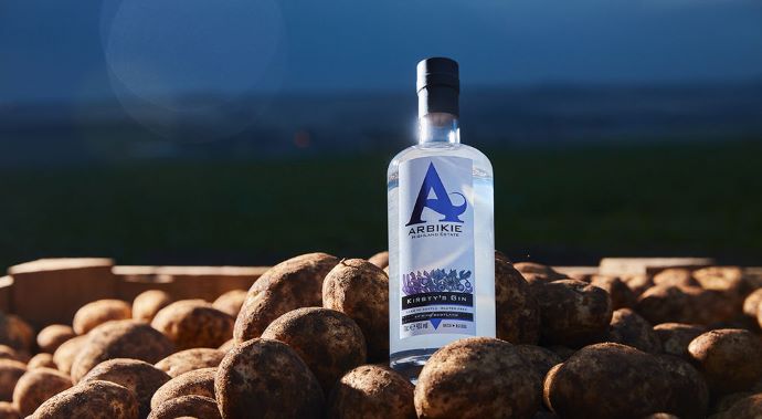 a bottle of kirsty's gin in a coastal setting on rocks with blue skies and seas
