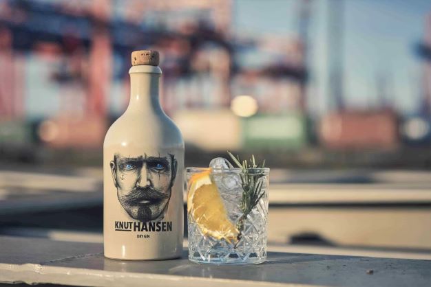A BOTTLE OF GIN WITH A GIN AND TONIC GARNISHED WITH HERBS