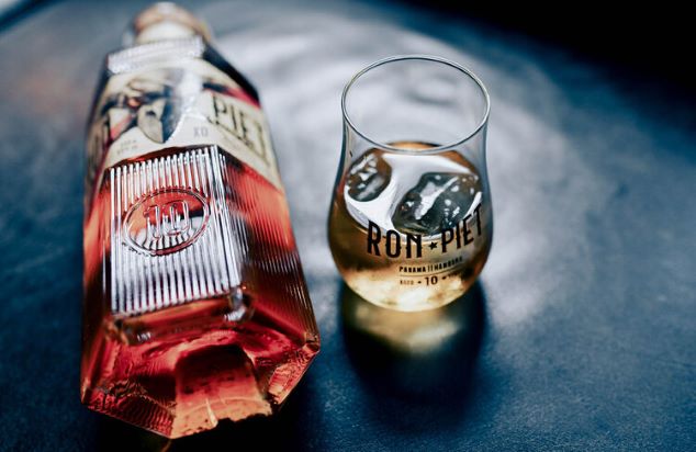 a bottle of rum laying on a black table with a shot of rum on ice