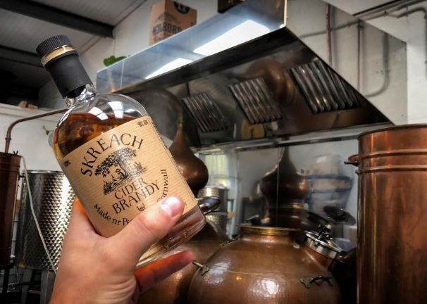 a bottle of skreach cider brandy held by a man in a distillery setting