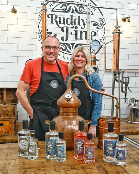 a man and a woman in a distillery setting holding bottles of gin