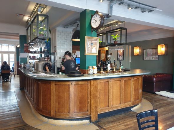 a curved wooden bar with tiled walls and a man serving