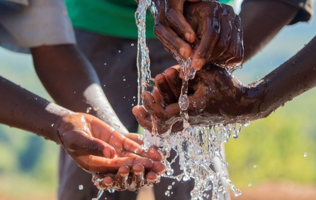 many hands being washed in water from a stand pump