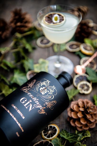 a bottle of brentingby black gin on a table with leaves citrus and a cocktail jigge