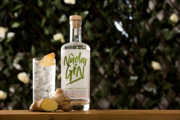 A BOTTLE OF NADAR GIN ON A TABLE WITH A GIN AND TONIC GARNISHED WITH FRESH GINGER