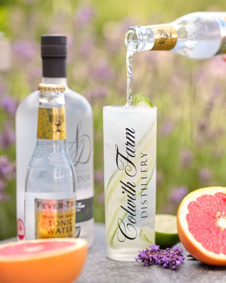 A GIN AND TONIC BEING POURED, GARNISHED WITH FRESH CITRUS AND GARDEN FLOWERS