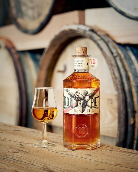 a bottle of rum on a wooden barrel with a shot of rum in a glass