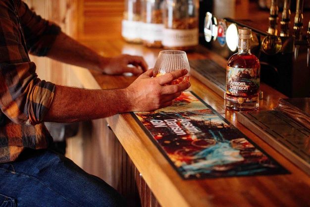 A MAN SITTING AT A BAR WITH A DRINK AND A BOTTLE OF GIN 