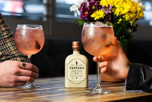 a bottle of gin on a wooden table being shared by a couple drinking gin and tonics