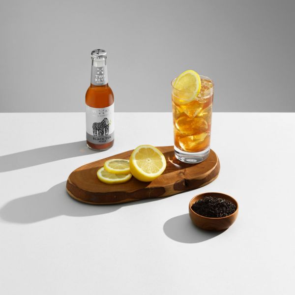 A BOTTLE OF TWO KEYS BLACK TEA MIXER WITH A WHISKY COCKTAIL ON A BLUE BACKGROUND